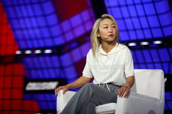 Sarah Guo | BetaKit Sarah Guo sits in a chair on stage with a mic on her face on a panel at Collision